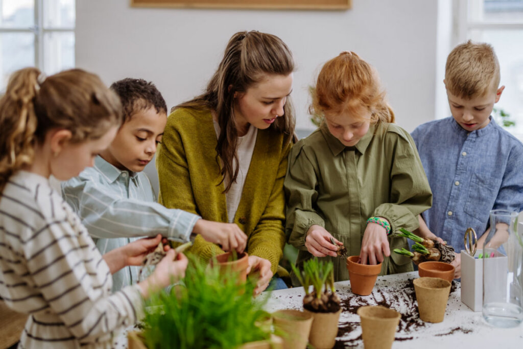 Professora ensinando crianÃ§as a cuidarem de pequenas plantas.