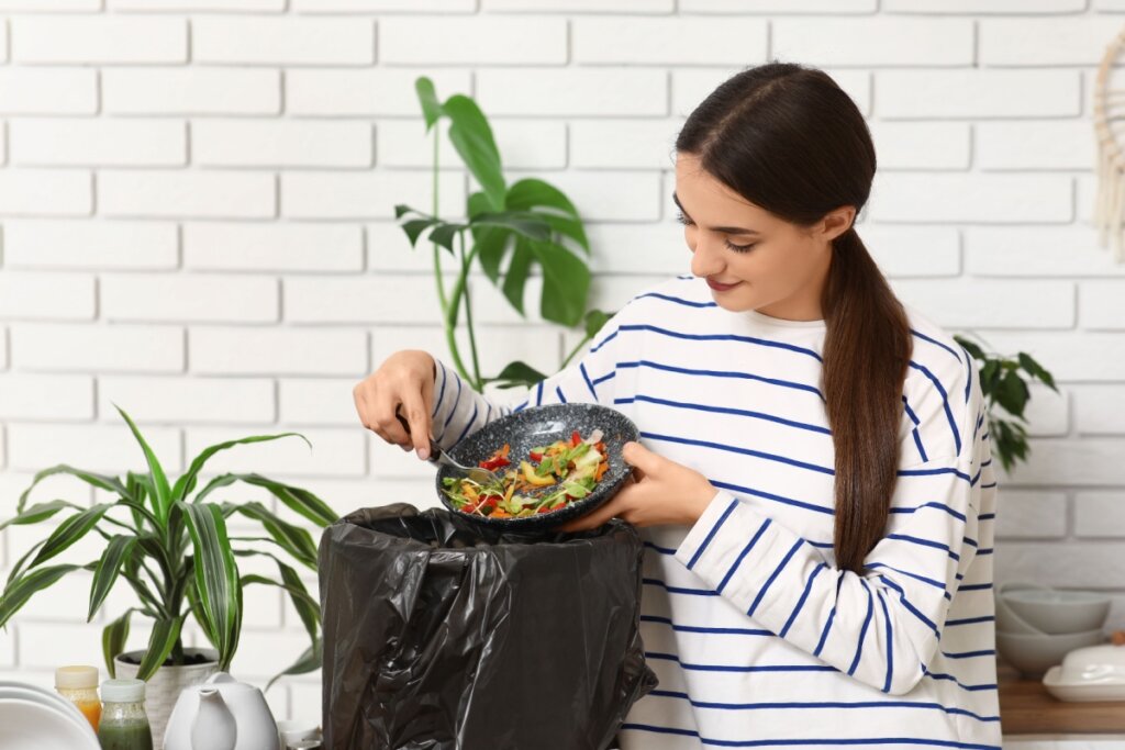 Mulher jogando sobras de comida org&acirc;nica em lixo org&acirc;nico com saco preto