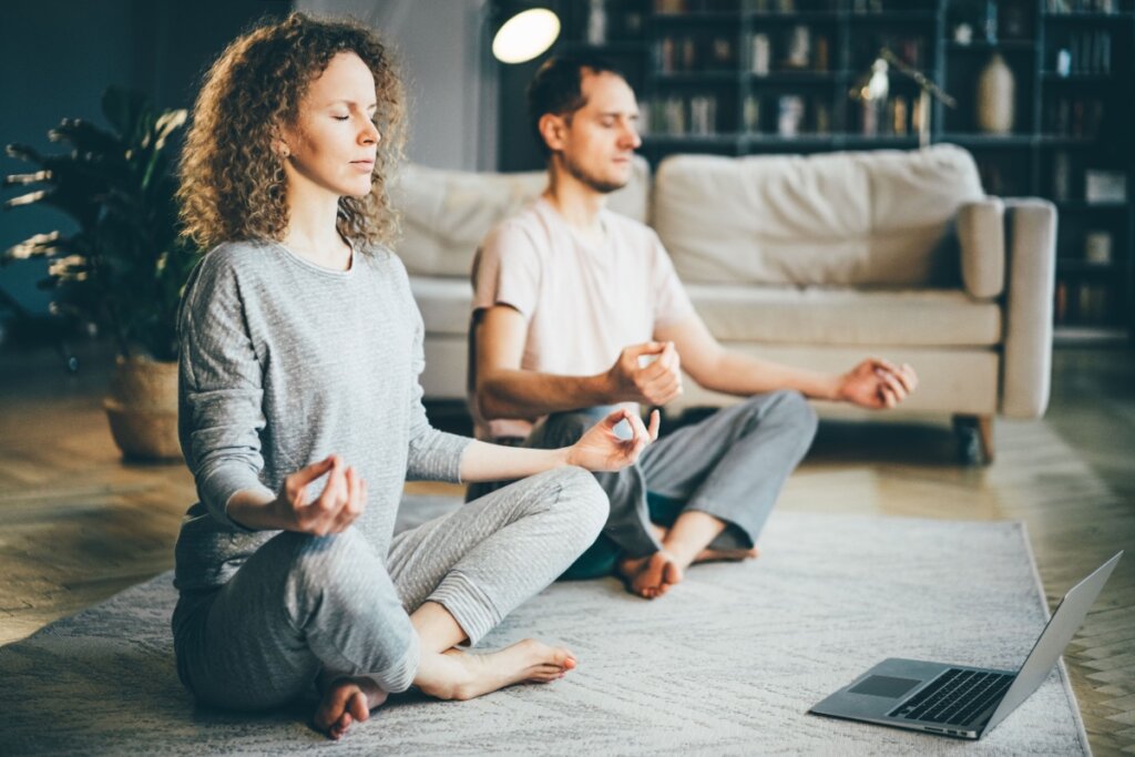 Homem e mulher meditando em posiÃ§Ã£o de lÃ³tus na sala, com olhos fechados
