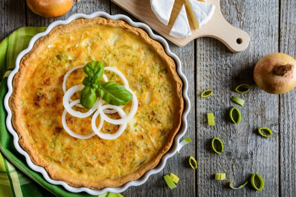 Quiche de alho-porÃ³ em refratÃ¡rio branco com rodelas de cebola e folhas de manjericÃ£o em cima