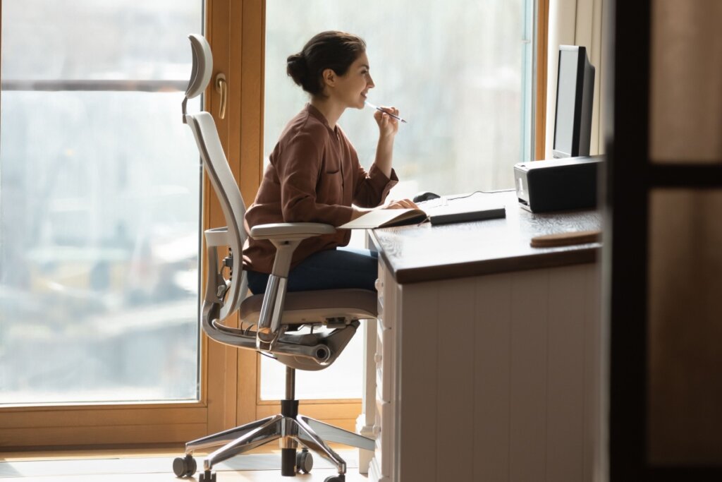 Mulher de cabelo preso sentada em cadeira ergonÃ´mica e de frente para monitor de computador