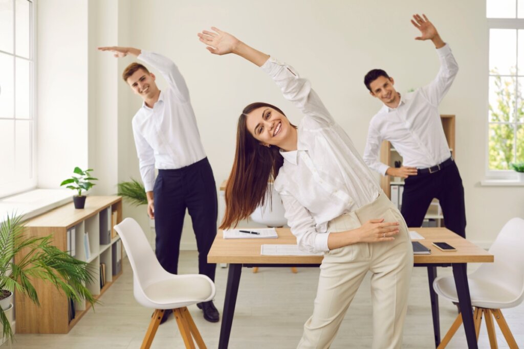 3 pessoas se alongando durante uma pausa no trabalho no escritÃ³rio, ambos estÃ£o usando roupas sociais