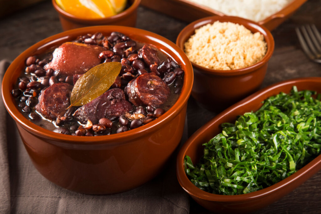 Feijoada em panela de barro ao lado de recipiente com couve e farofa