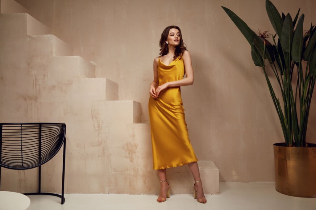 Mulher com vestido de festa amarelo posando para foto ao fundo uma escada