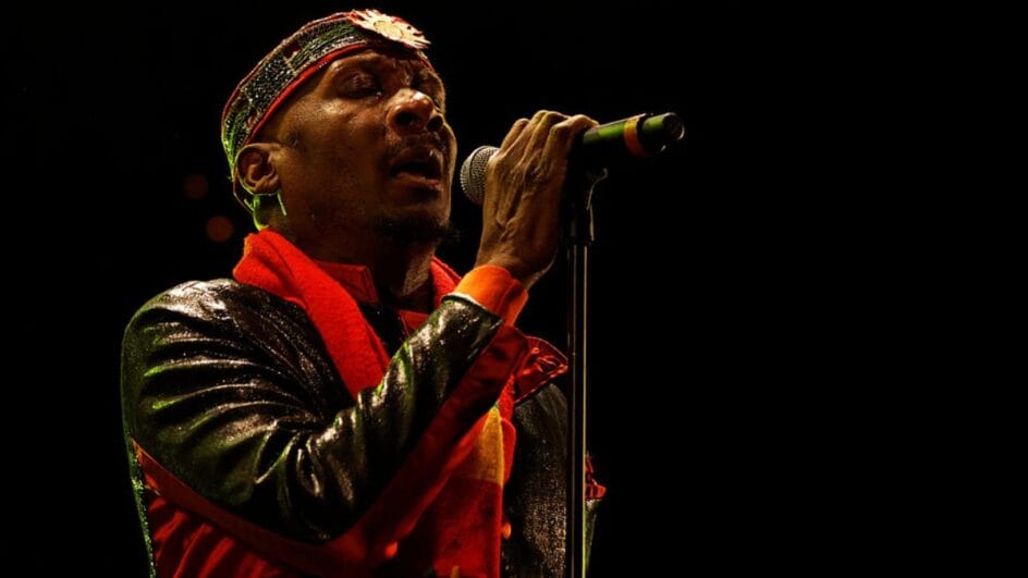 O cantor Jimmy Cliff sorrindo enquanto canta e toca violão em um show, simbolizando seu legado no reggae.