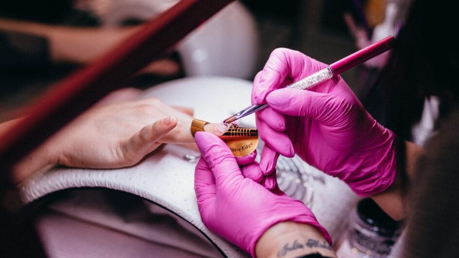 Foto mostra uma manicure fazendo as unhas de uma cliente