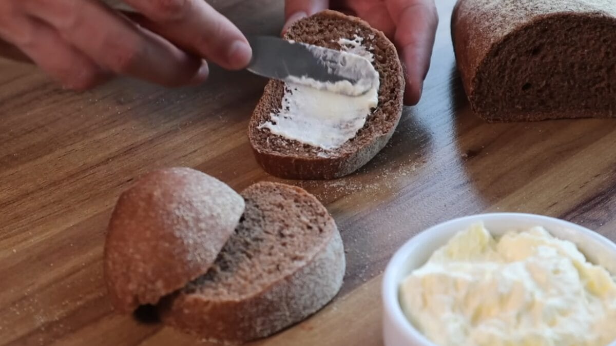 Pessoa espalhando manteiga em fatia de pão australiano de coloração escura