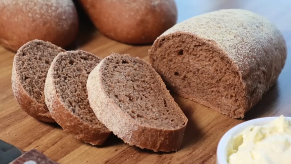 Fatias de pão australiano, de coloração escura, sobre tábua de madeira