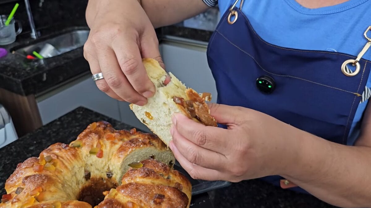 Mulher abrindo com as mãos pedaço de rosca, massa assada com frutas cristalizadas