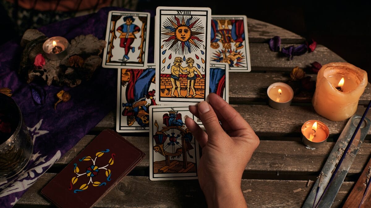 Imagem de pessoa segurando a carta de tarô O Sol com a mão direita, sobre uma mesa onde outras cartas estão dispostas