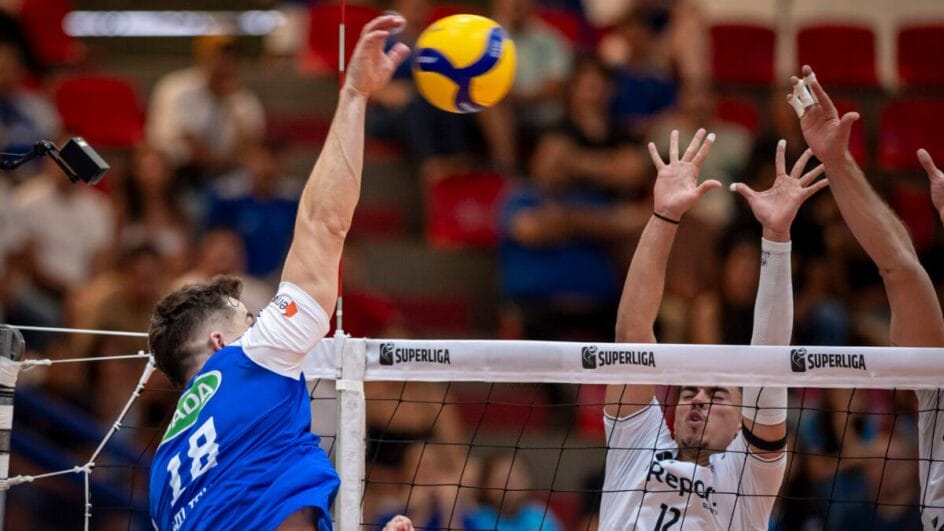 Atleta do Cruzeiro atacando bola por cima da rede com dois jogadores do Suzano no bloqueio pela Superliga Masculina 202526