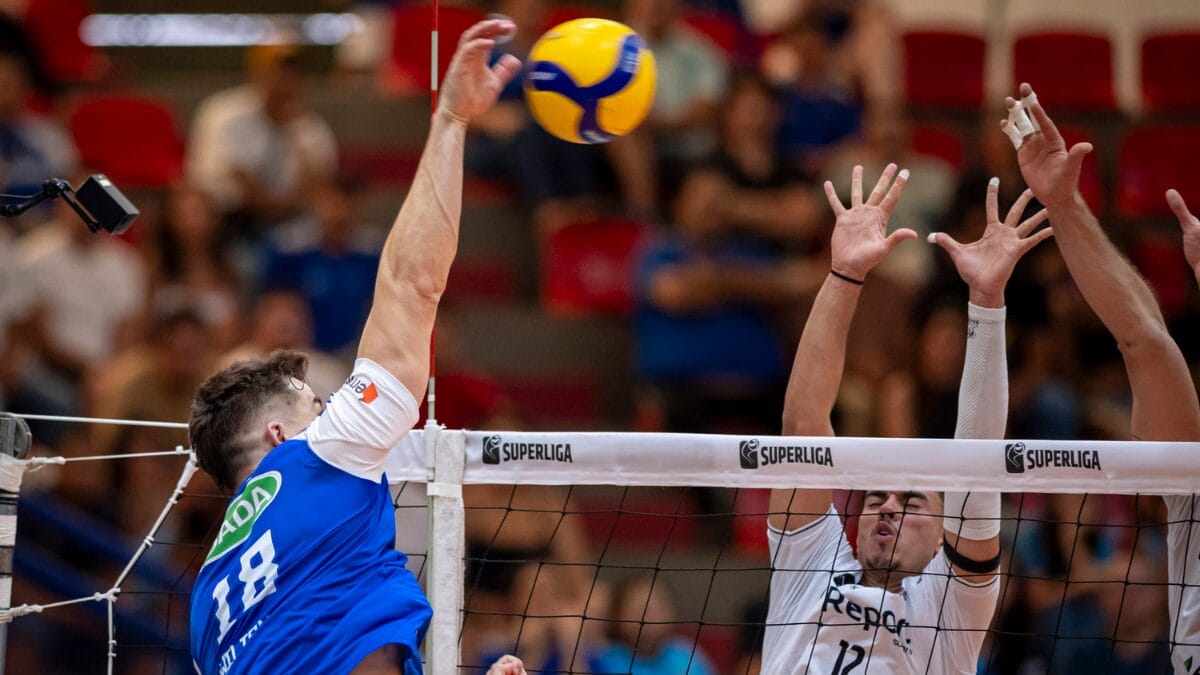 Atleta do Cruzeiro atacando bola por cima da rede com dois jogadores do Suzano no bloqueio pela Superliga Masculina 202526