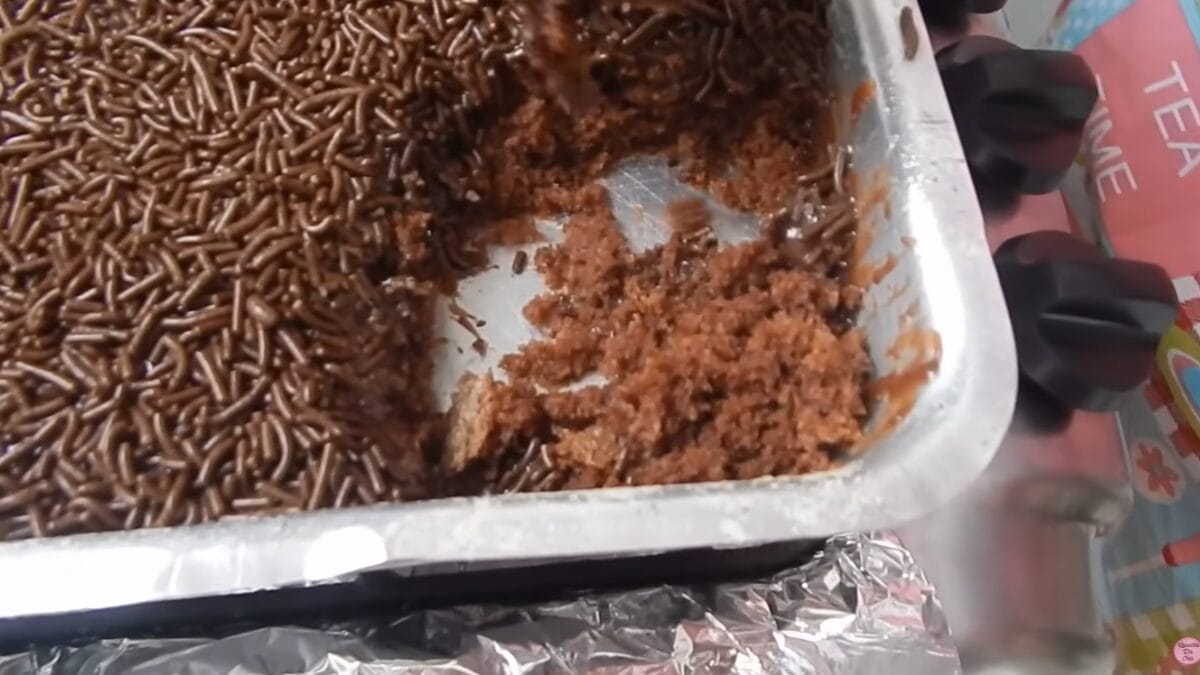 Assadeira com bolo de chocolate já cortado, mostrando a massa úmida e cobertura com granulado.