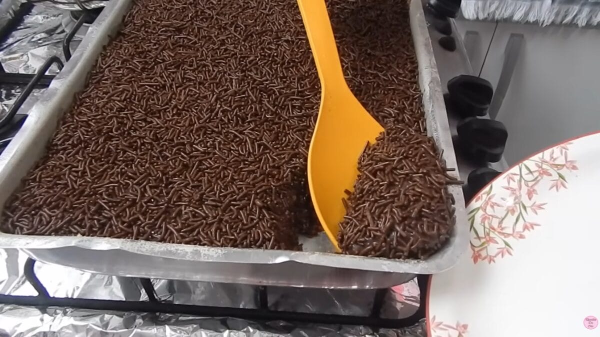 Colher retirando porção de bolo de chocolate com cobertura e granulado direto da assadeira.