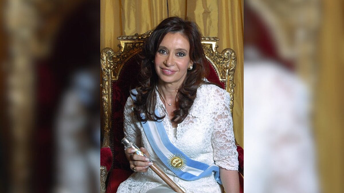 Foto mostra Cristina Kirchner, ex-presidente da Argentina, sentada em uma cadeira sorrindo.