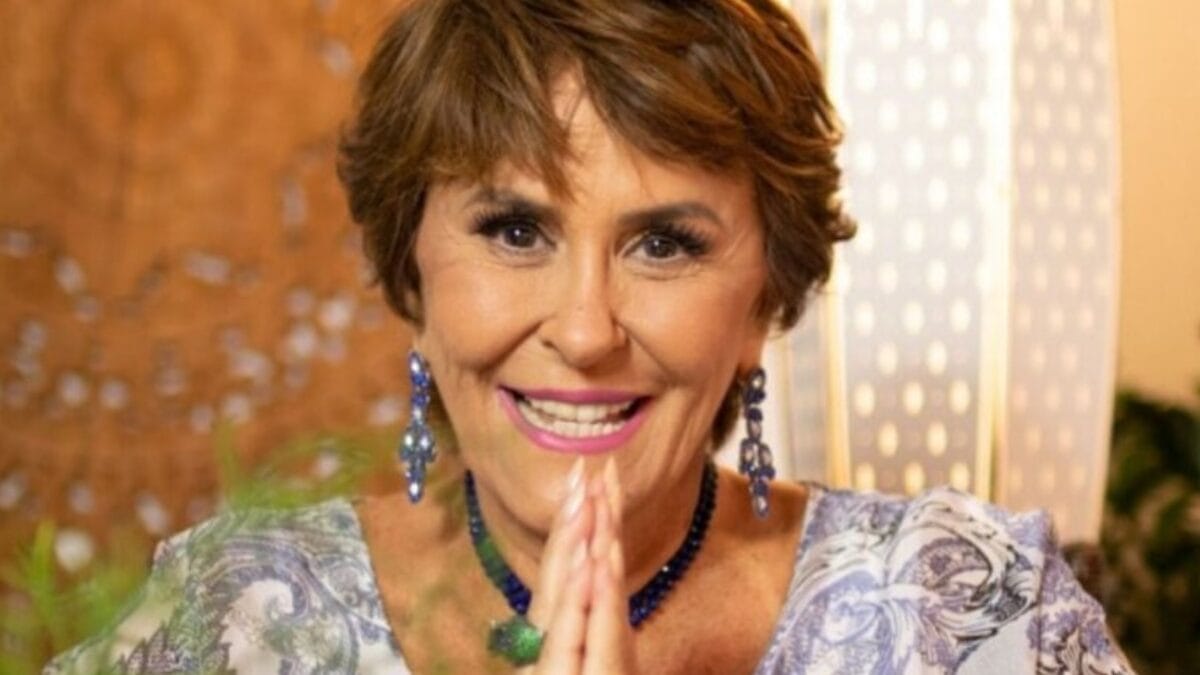 Astróloga Márcia Sensitiva aparecendo sorridente, com as mãos unidas e acessórios azuis.