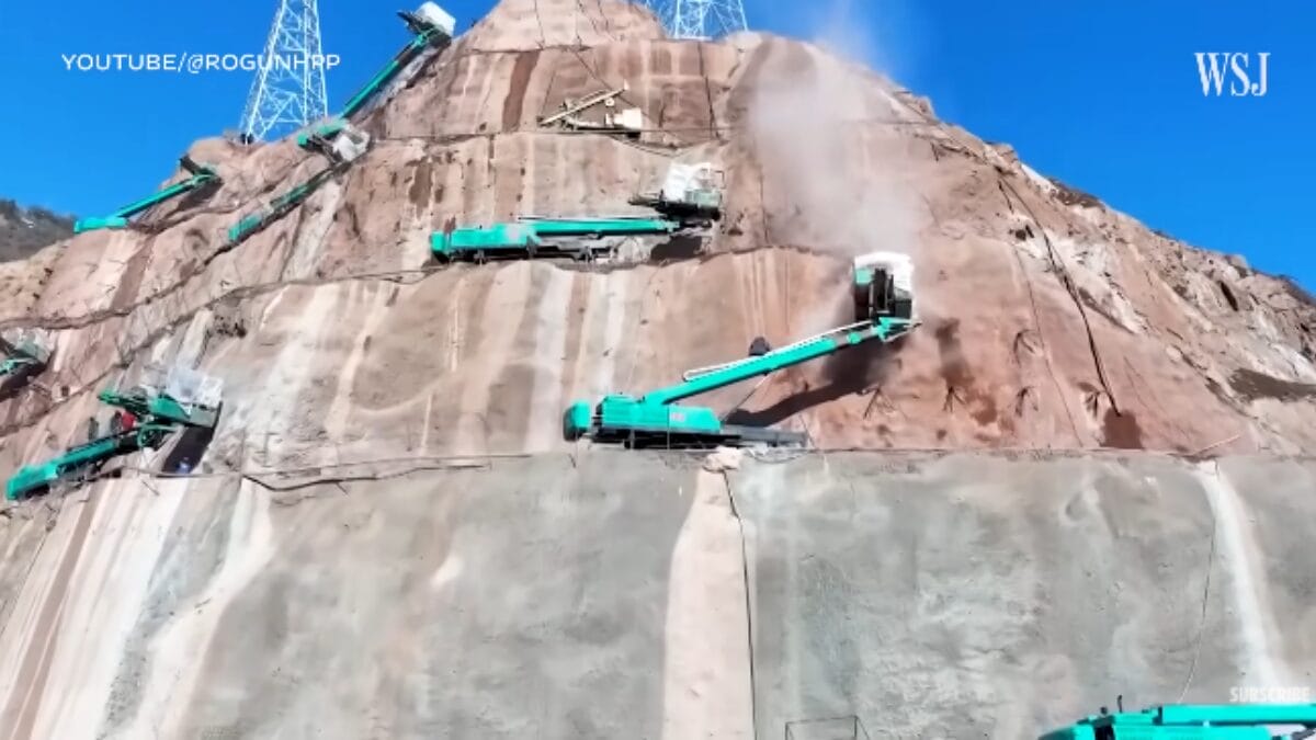 Máquinas de construção de cor ciana trabalhando na perfuração e estabilização de uma encosta rochosa íngreme.