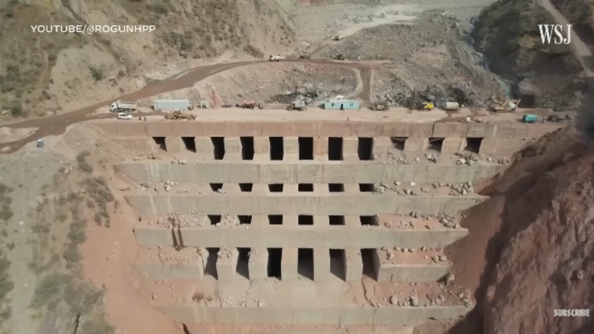 Grande estrutura de concreto em construção com várias aberturas quadradas dispostas em fileiras, localizada em um desfiladeiro.