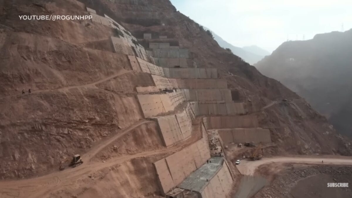 Grandes estruturas de concreto e terra na encosta de uma montanha árida, parte da construção da barragem de Rogun.