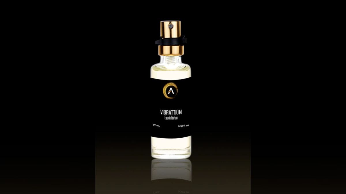 Frasco pequeno e cilíndrico de perfume da marca "Vibrattion" (Eau de Parfum, 17ml). O frasco é de vidro transparente com etiqueta preta minimalista e tampa dourada, fotografado contra um fundo preto com iluminação dramática.