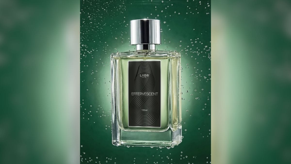 Frasco de vidro retangular e transparente do perfume "Effervescent" da marca Lab 8 Niche. A imagem tem um fundo verde escuro com gotículas de água em suspensão e iluminação traseira, destacando o líquido esverdeado e a tampa prateada.