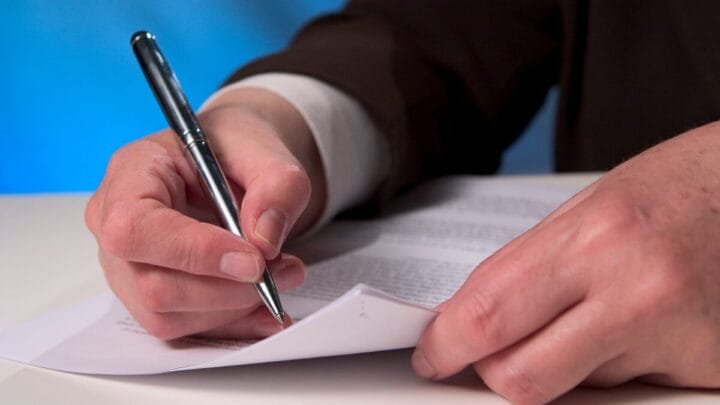 A foto mostra um estudante escrevendo em uma prova