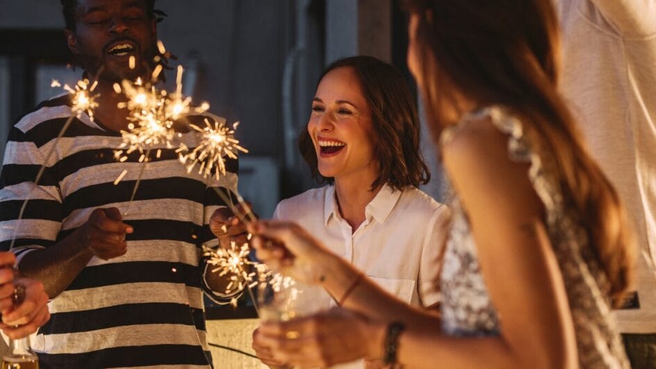 Grupo de amigos comemorando com velas de faísca, clima de festa e celebração entre adultos sorrindo à noite.