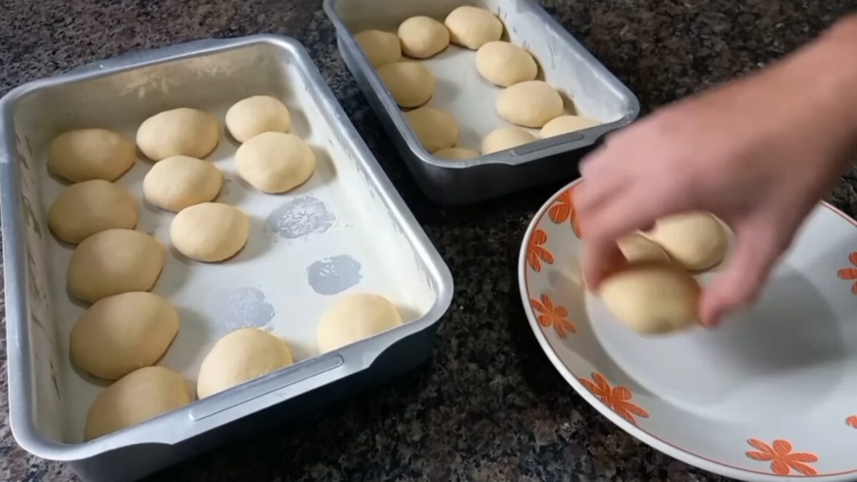 Pedaços de massa de bolacha caseira sendo colocados em um prato decorado, ao lado de formas com mais unidades cruas.