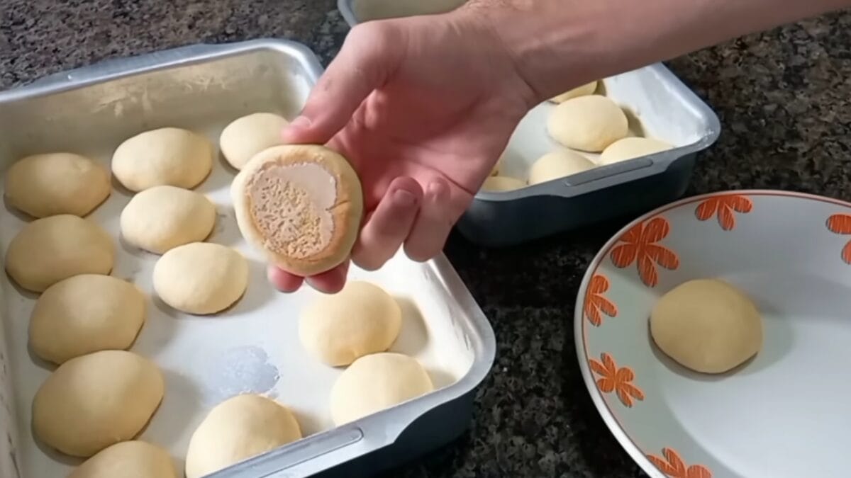 Mão segurando uma bolacha caseira mostrando o fundo levemente dourado, ainda na forma com outras unidades.
