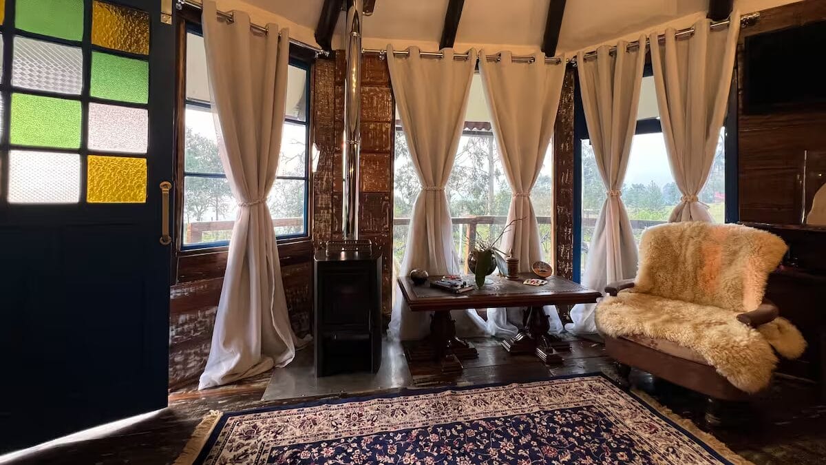 Interior de cabana rústica com lareira, cortinas claras e decoração aconchegante em meio à natureza de SC.