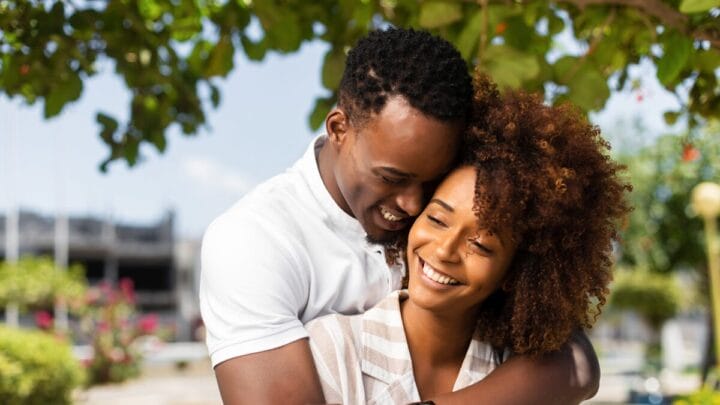 Casal sorrindo em abraço carinhoso ao ar livre, representando relacionamento saudável e afeto.