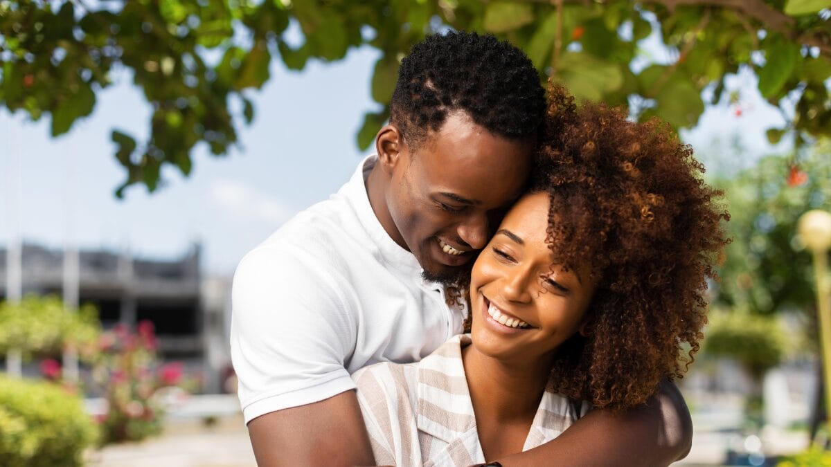 Casal sorrindo em abraço carinhoso ao ar livre, representando relacionamento saudável e afeto.