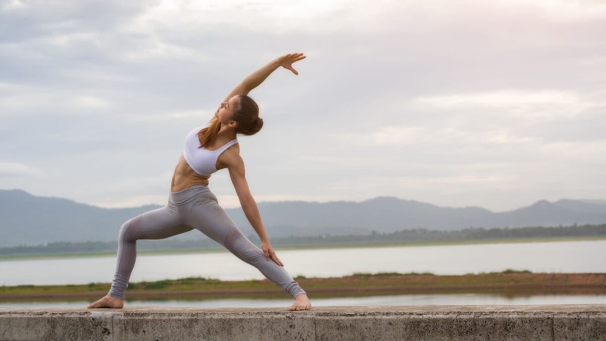Mulher fazendo alongamento de yoga ao ar livre, atividade física voltada para flexibilidade e bem-estar.