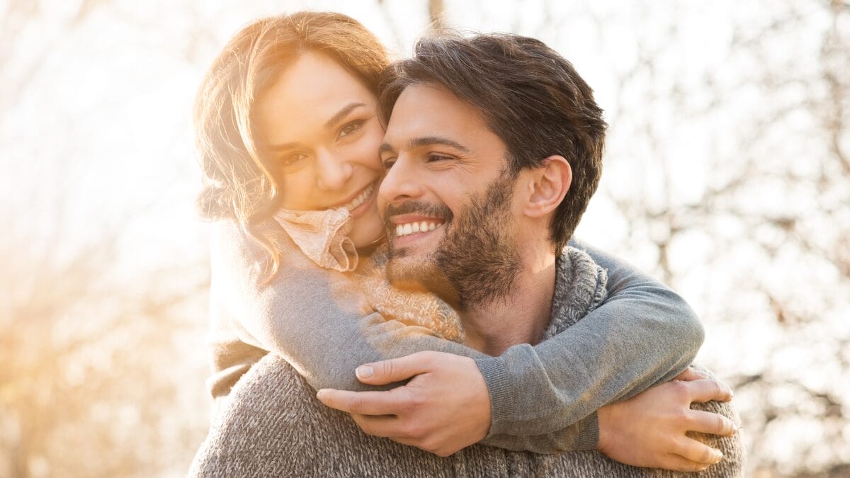 Casal sorrindo em abraço carinhoso ao ar livre, momento de afeto e relacionamento saudável.