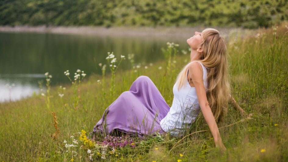 Mulher sentada na grama ao lado de flores silvestres curtindo a natureza, foco em tranquilidade e autocuidado.