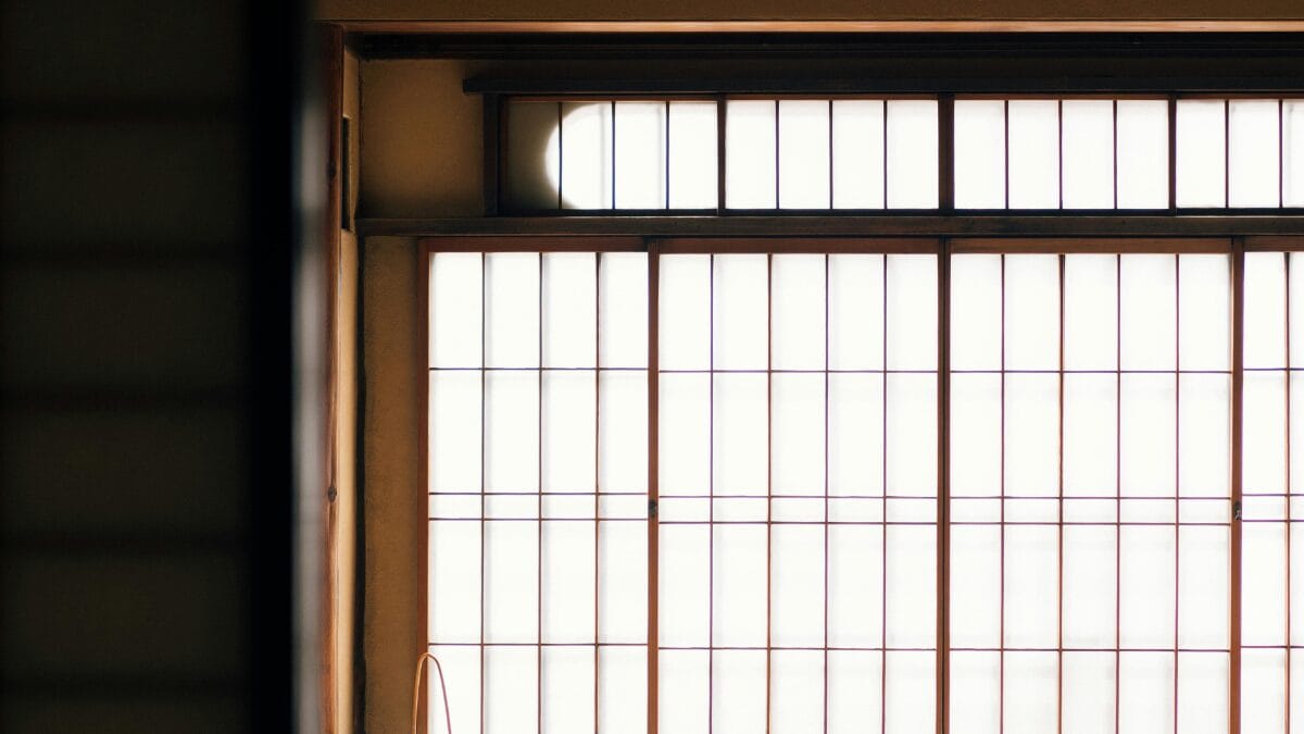 Parede composta por pain&eacute;is shoji fechados. A forte luz natural externa atravessa o papel de arroz, destacando a silhueta das grades de madeira escura e criando um brilho suave e difuso no interior.