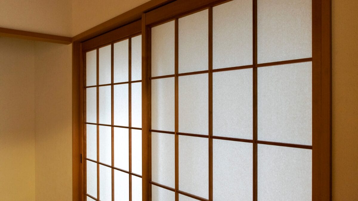 Close-up em &acirc;ngulo de duas portas de correr japonesas (shoji). As estruturas s&atilde;o de madeira clara com pain&eacute;is retangulares de papel branco transl&uacute;cido, mostrando a textura suave do material.