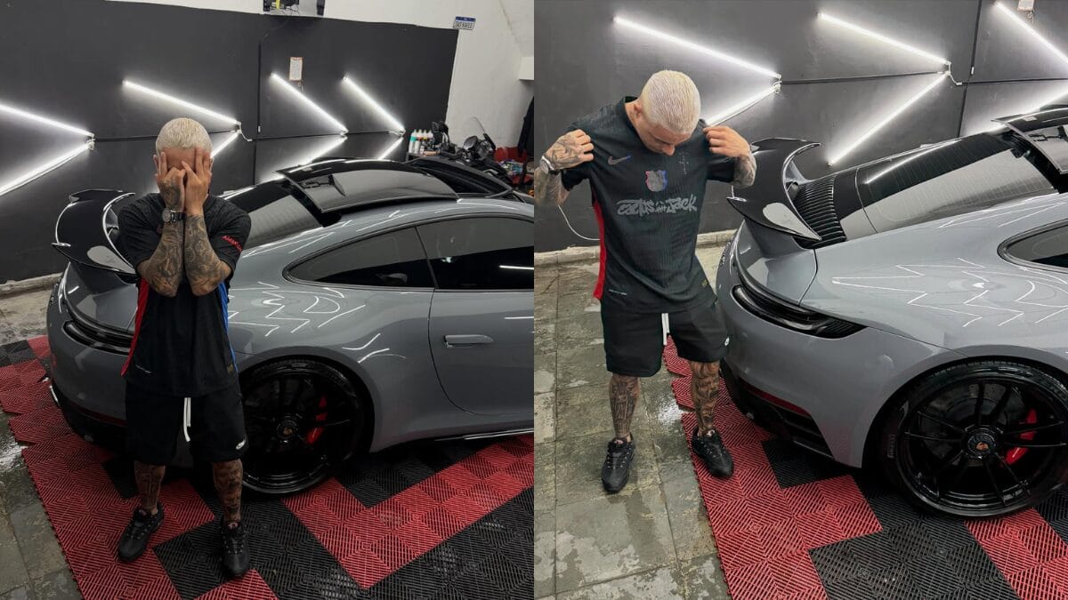 MC Tuto posa ao lado de um Porsche 911 cinza em uma oficina de est&eacute;tica automotiva. Ele veste uma camiseta preta da colabora&ccedil;&atilde;o "Cactus Jack". O carro possui rodas pretas e pin&ccedil;as de freio vermelhas.