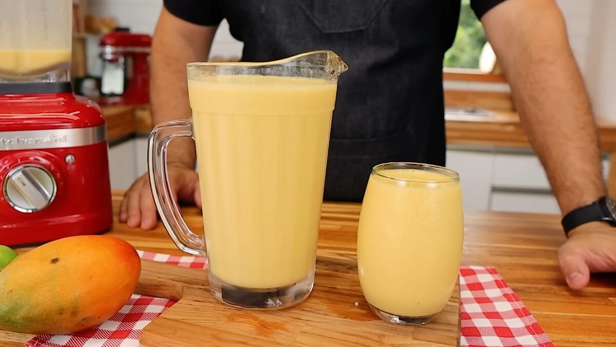 Jarra e copo de limonada alemã cremosa sobre bancada de madeira, com limões ao lado e liquidificador ao fundo