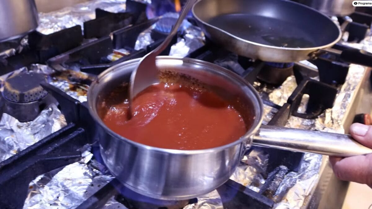 Panela com molho de tomate caseiro sendo mexido durante preparo em cozinha profissional