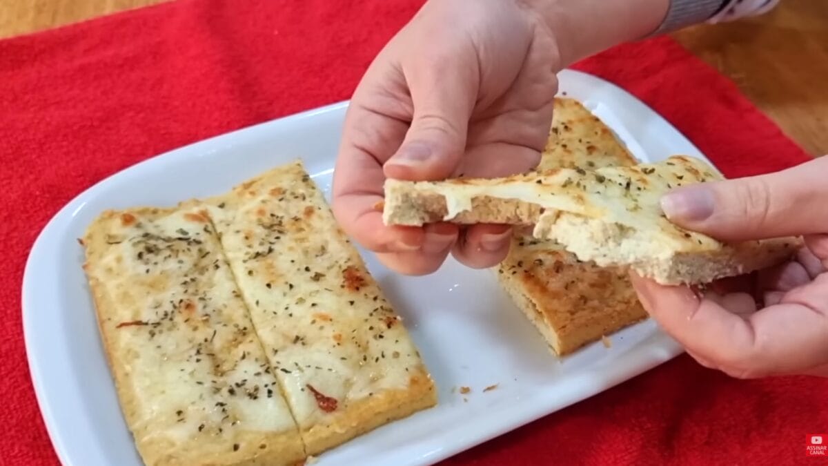 Mãos seguram fatia de pão sem carboidratos com cobertura derretida destacando a textura