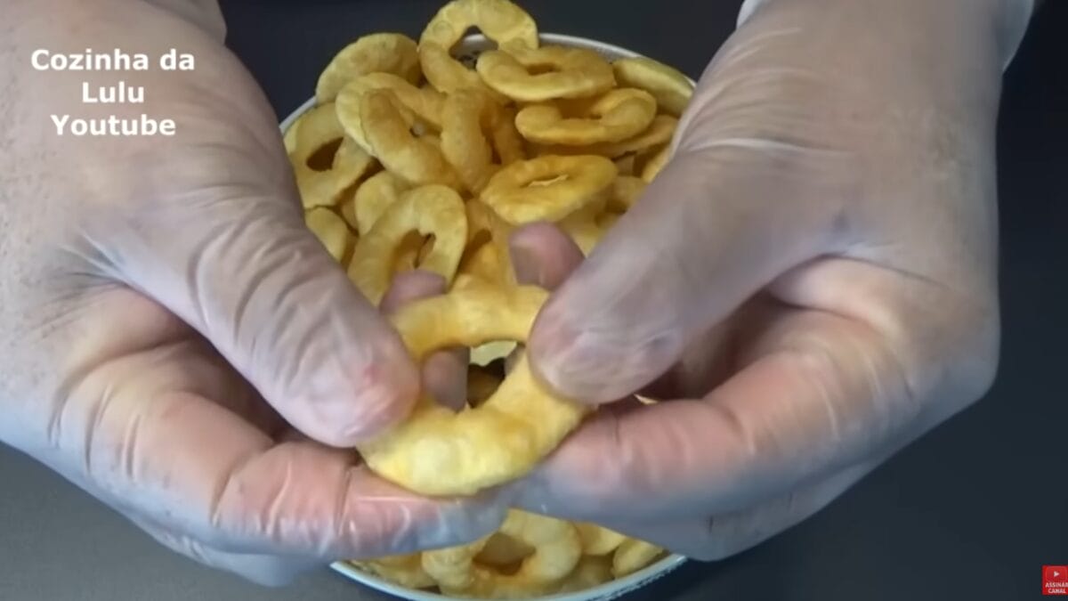 Salgadinho frito sendo segurado com as mãos mostrando crocância e formato em anel