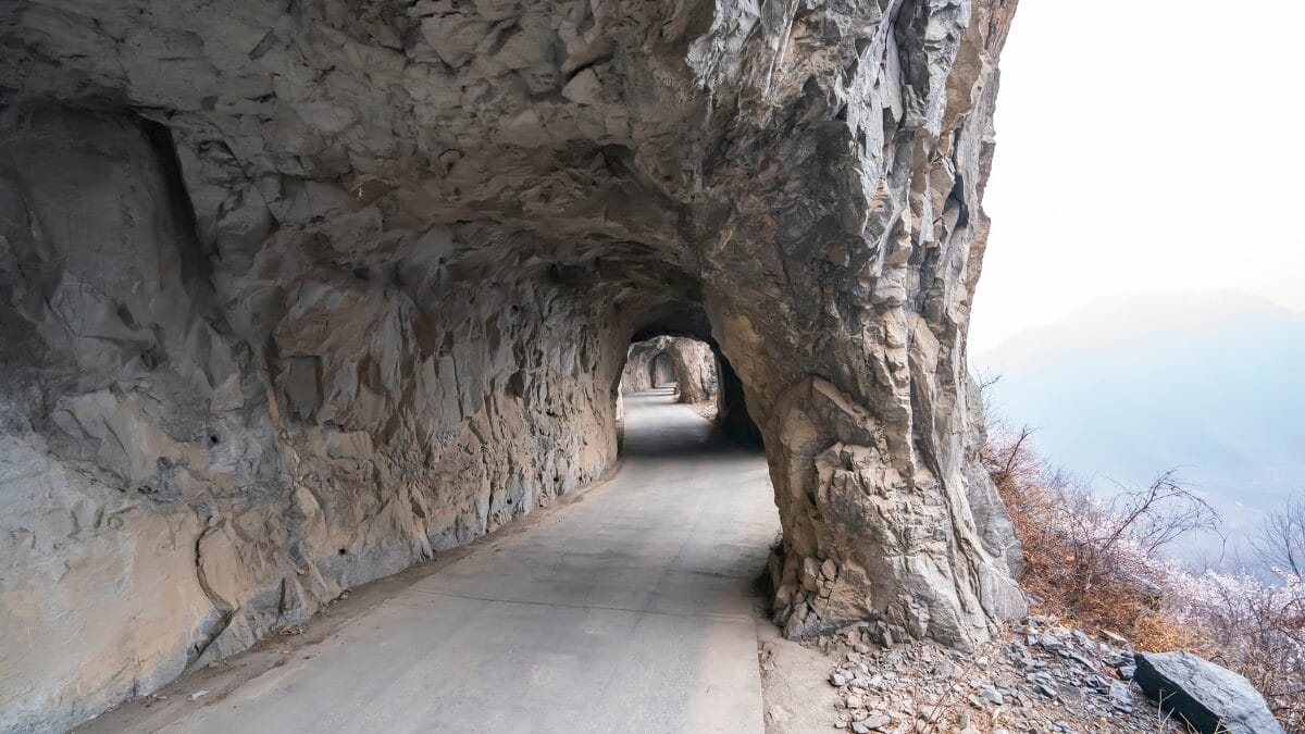 Perspectiva de dentro do t&uacute;nel olhando para a frente. Uma grande "janela" escavada na rocha &agrave; direita revela a n&eacute;voa e a paisagem montanhosa l&aacute; fora.