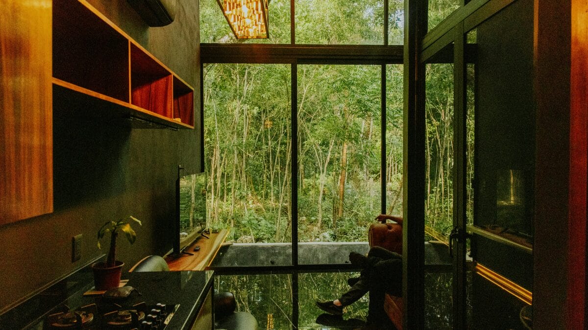 Cozinha com paredes escuras e grandes janelas de vidro voltadas para uma &aacute;rea verde, integrando o ambiente interno &agrave; natureza.