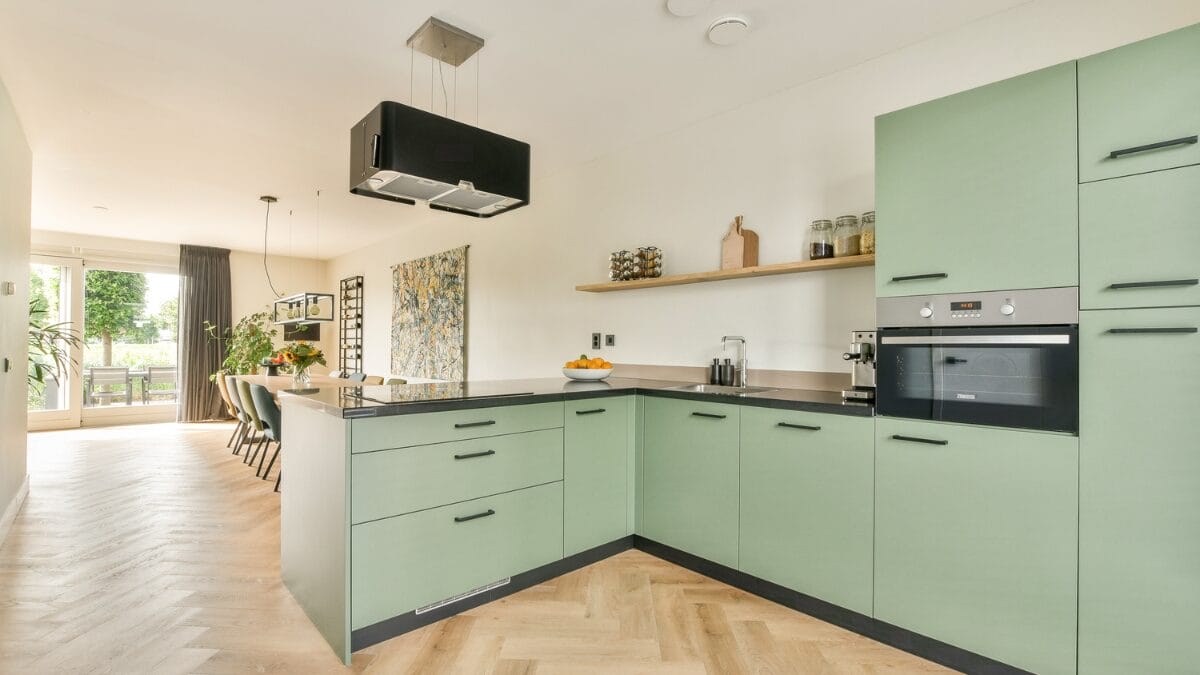 Cozinha moderna com ilha central, arm&aacute;rios verde oliva e detalhes em madeira clara.