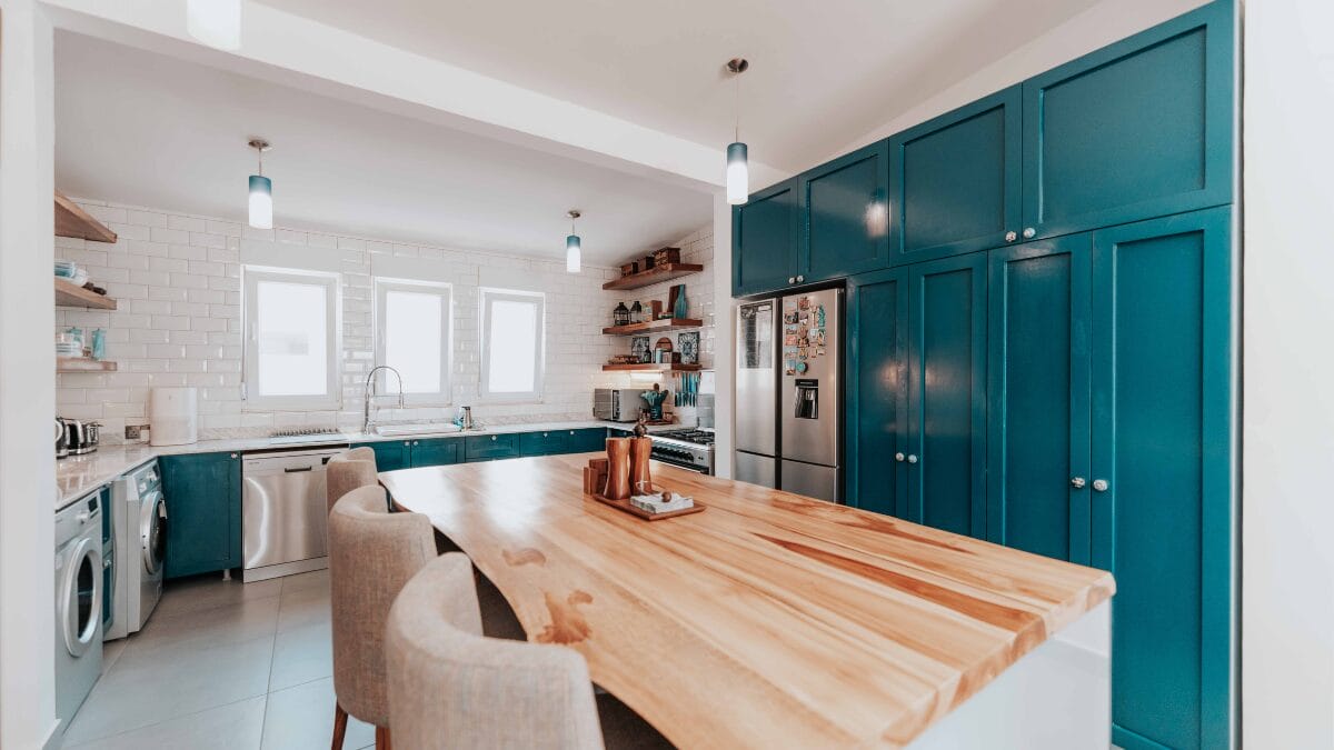 Cozinha ampla com arm&aacute;rios verde escuro, bancada de madeira e eletrodom&eacute;sticos embutidos.