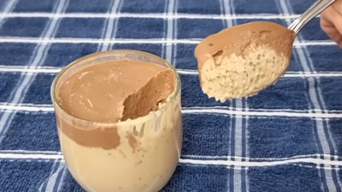 Colher retirando camada cremosa de cacau de café da manhã anti-inflamatório com chia e iogurte