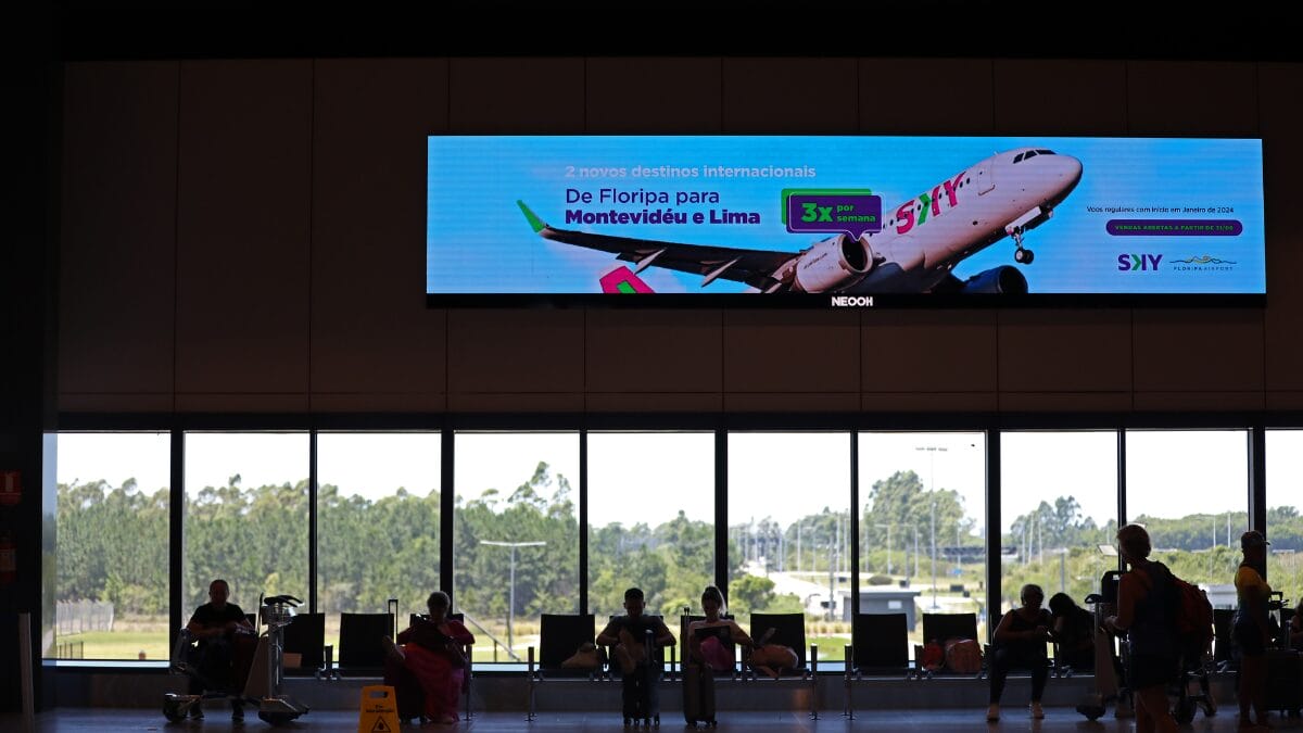 Passageiros aguardam voos no saguão do Aeroporto Internacional de Florianópolis, em área ampla e iluminada.