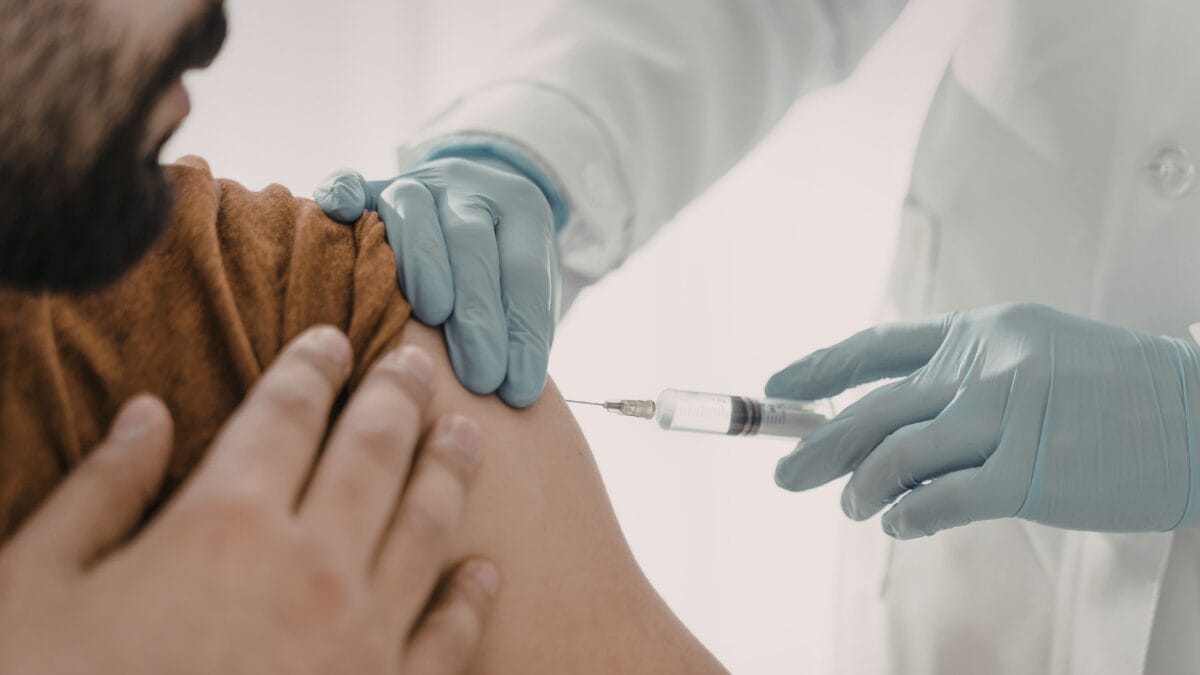 Profissional da sa&uacute;de utiliza luvas e aplica vacina em paciente.
