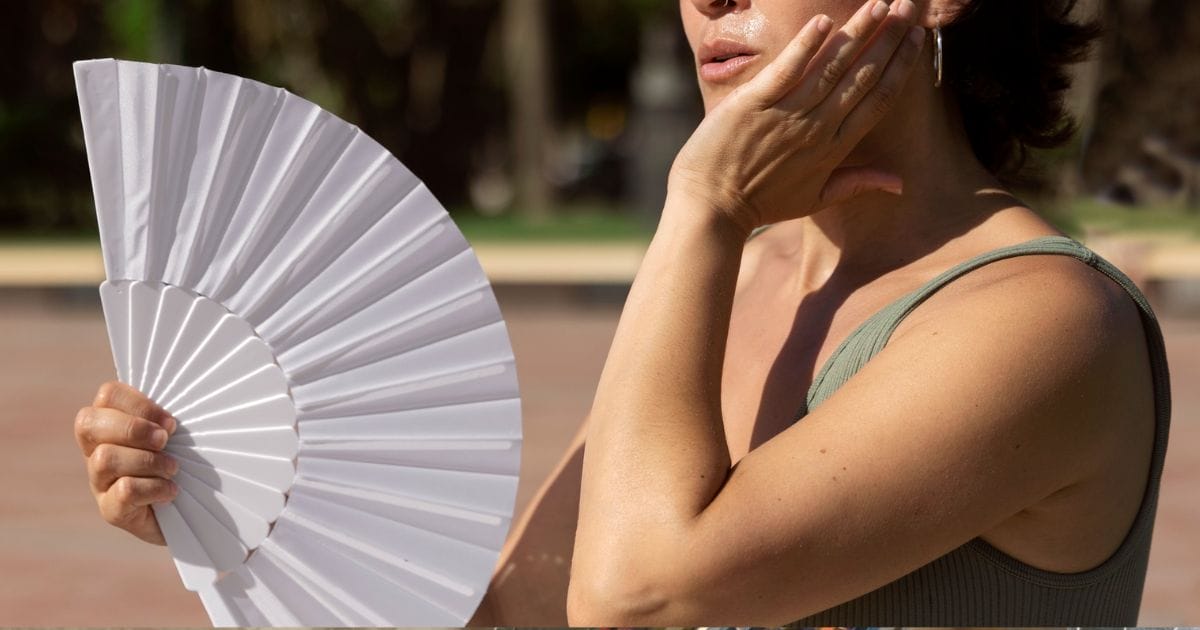 Mulher se abanando com leque para se refrescar no calor intenso